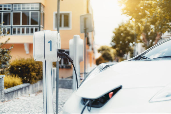 Electric vehicle plugged into a white charging station on a residential street